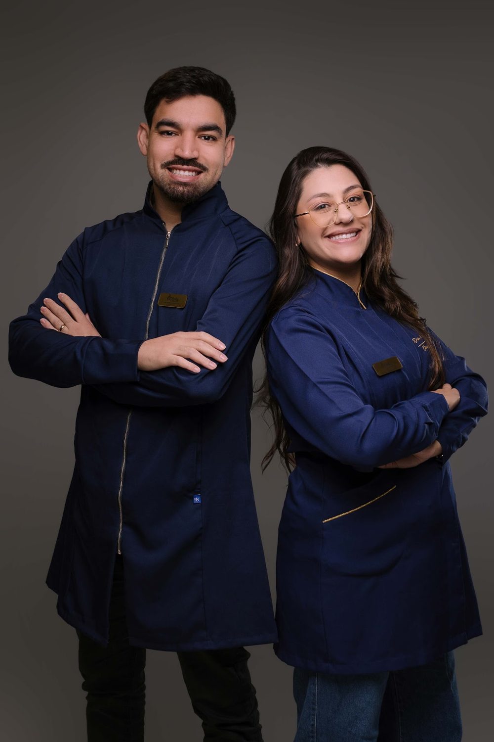 Dois profissionais da iClinic de braços cruzados, com jalecos azul-marinho